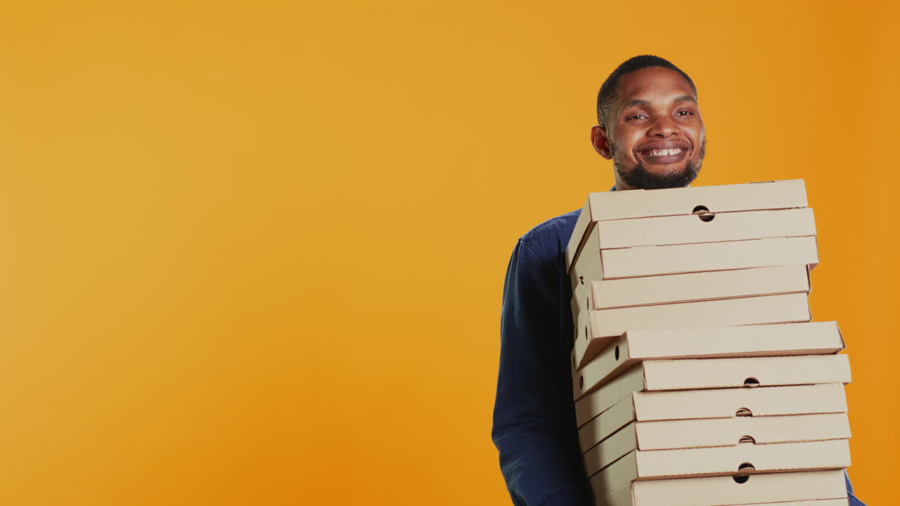 Confident male courier carrying big pile of pizza boxes to deliver fast food order