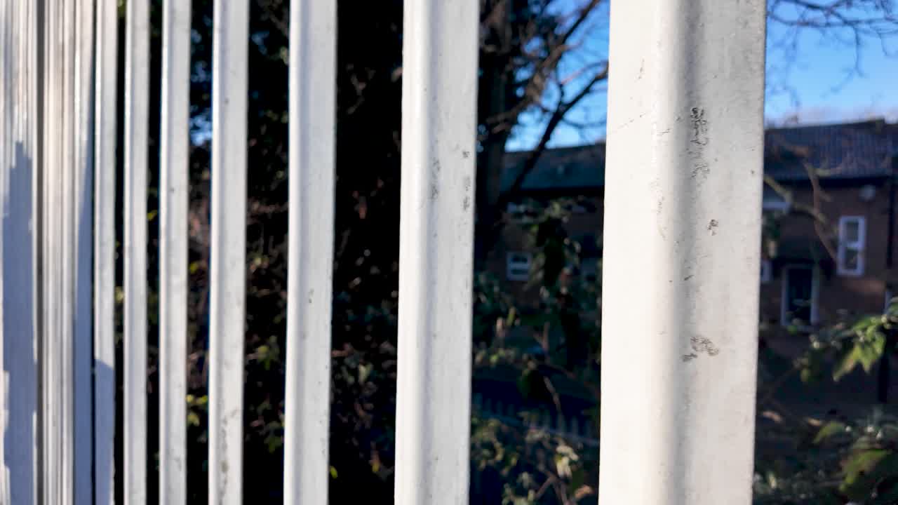 Ringhiere in metallo bianco sulla piattaforma della stazione ferroviaria con edificio e alberi sullo sfondo in una giornata di sole per concetti di trasporto e scenari urbani