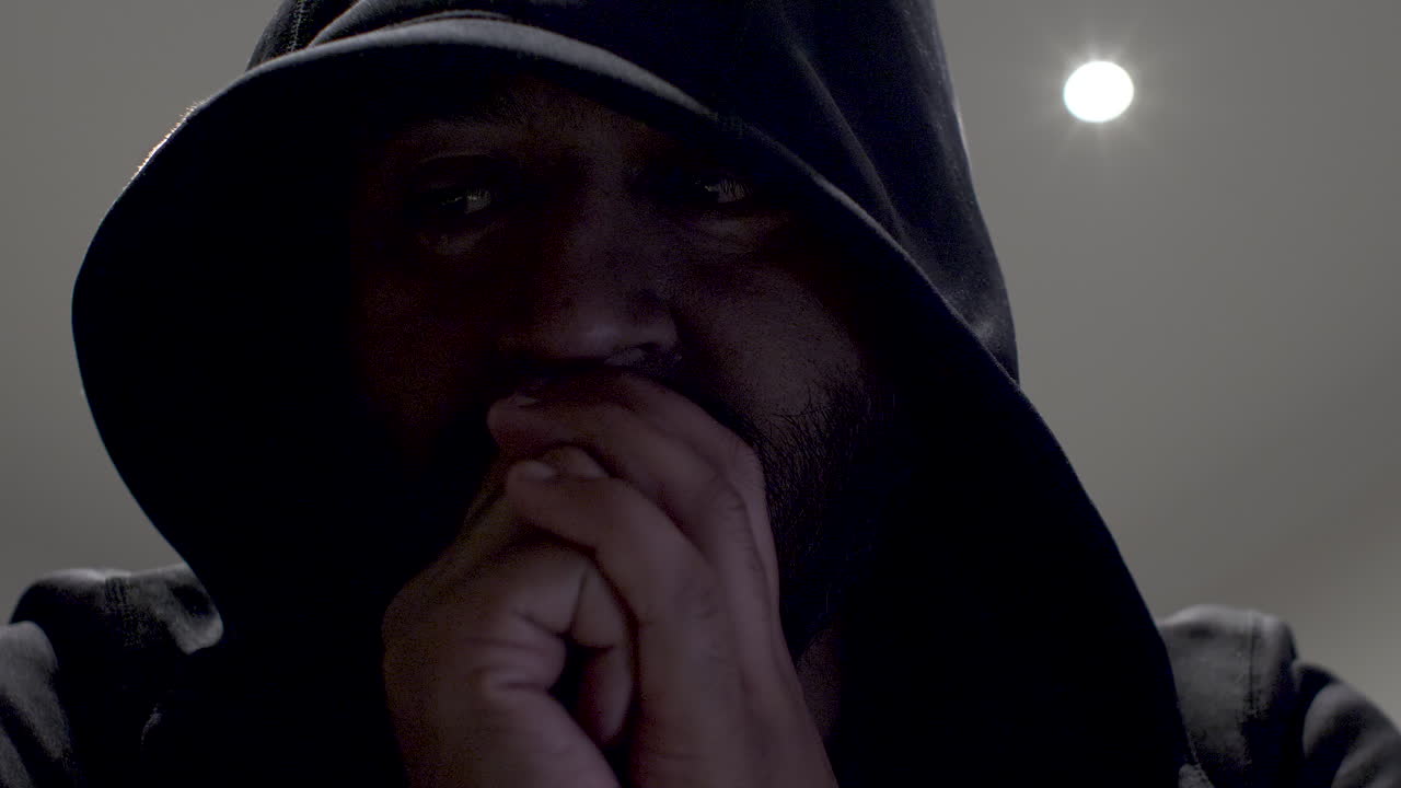 hooded mann med sammenklemte hender rocker frem og tilbake