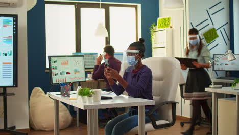 mujer negra navegando en el teléfono inteligente sentada en una nueva oficina normal