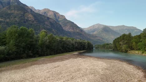 a slow forward drone pan over the rocky bottom of the toce river, with trees, mountains, and sky creating a serene landscape in ansola, italy.