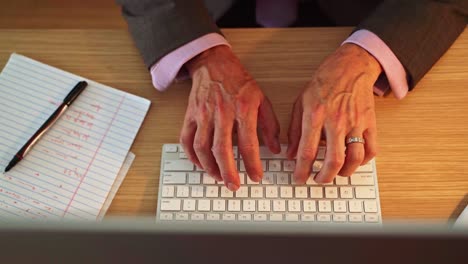 Business-man-in-a-suit-using-an-apple-iMac-computer-for-work-while-writing-down-notes-on-a-notepad