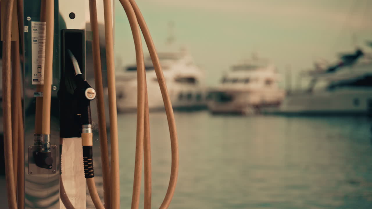 Various hoses coloured in yellow, green, and blue, hang beside modern marina fuel pumps, boat at the fuel station