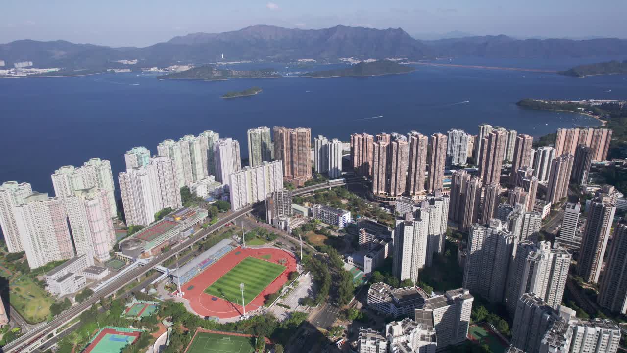 campo de fútbol y pista de atletismo entre los altos rascacielos poblados de vista paradiso mientras un tren se mueve sobre la vía férrea en hongkong