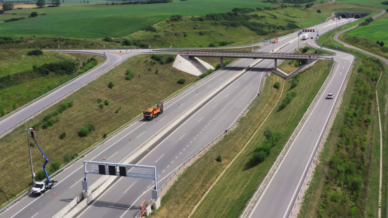 Aerial view of a highway with twin tunnels and an overpass surrounded by green fields
