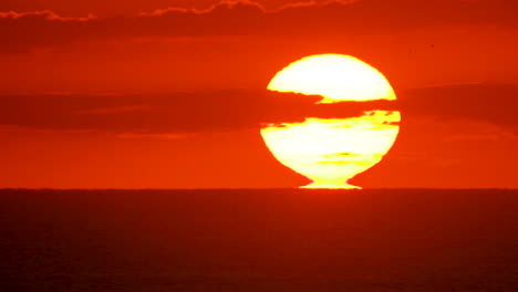 primer plano de un amanecer mientras el sol se aleja del horizonte del océano, iluminando el cielo naranja y rosa