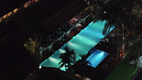 drone flight over thailand hotel resort with azure blue pool with palms at night