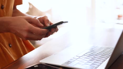 mujer caucásica usando una computadora portátil y su teléfono en casa