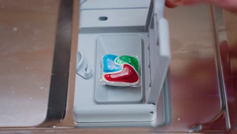 Man-putting-detergent-tablet-into-dishwasher