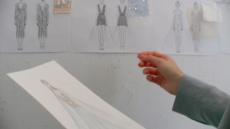 female fashion designer is choosing and hanging clothing sketches to wall for her newest collection. light fabrics. female fashion designer is choosing and