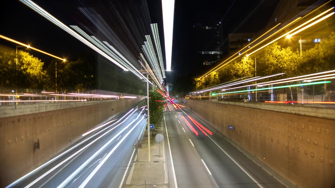 Rekaman timelapse lalu lintas malam hari di Barcelona dengan jejak cahaya warna-warni dari kendaraan.