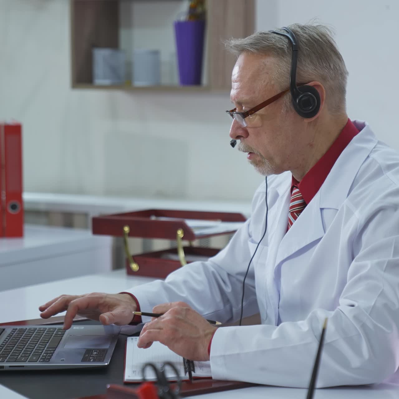 Doctor writing an appointment for a client during video call. Professional doctor with headphones making online consultation through the laptop in medical center.
