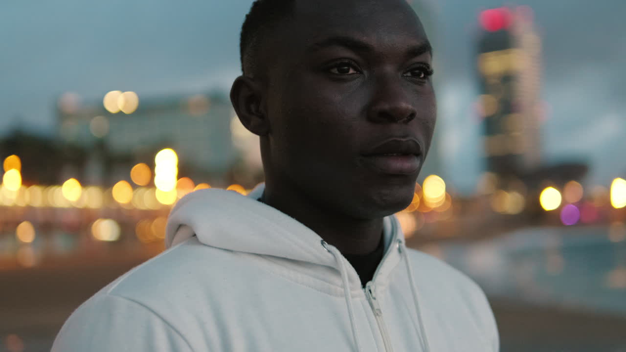Thoughtful Young Black Man Looking Out at City Lights at Dusk