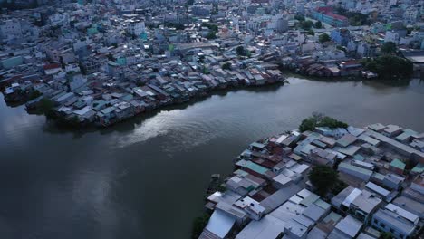 Aerial-panning-shot-of-urban-canal,-reflection-and-high-density-waterfront-housing-and-factories-in-Ho-Chi-Minh-City,-Vietnam-in-afternoon-light