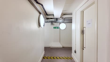 empty basement corridor in an office building with bright circular lights and visible pipes, creating a sterile and deserted atmosphere