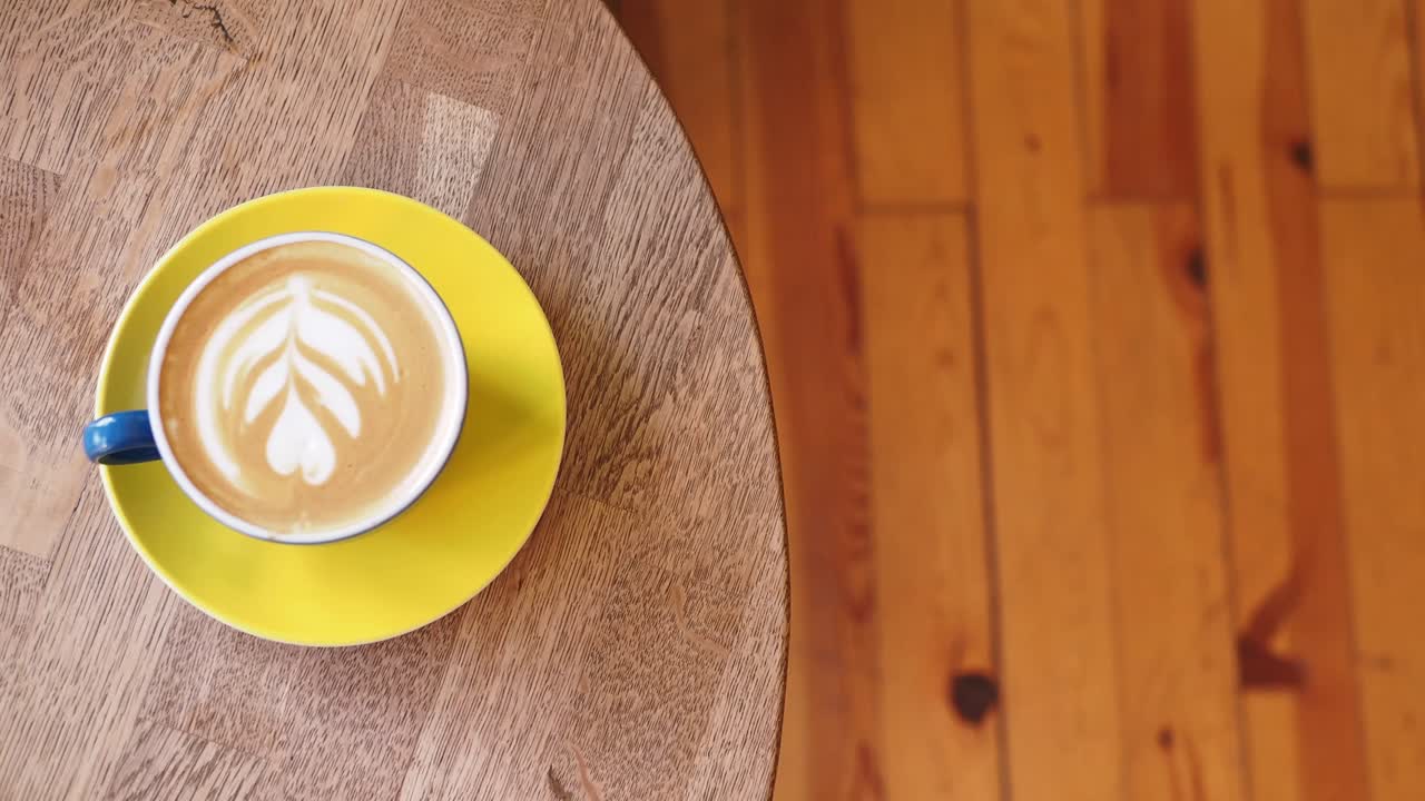Coffee latte on a wooden table with a hand reaching for it