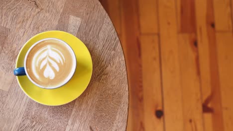 coffee latte on a wooden table with a hand reaching for it