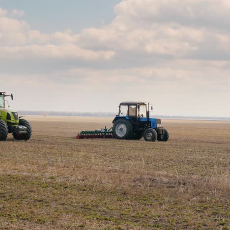 Steadicam-Shot:-Two-Tractors-With-Seeders-Sow-Wheat-On-The-Field-In-Early-Spring