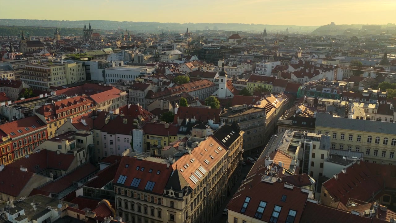 Vista aerea con drone su fitti tetti storici in tegole rosse con guglie di chiese gotiche e le torri gemelle della Chiesa di Tyn visibili nella mattinata nebbiosa, Praga, Repubblica Ceca.