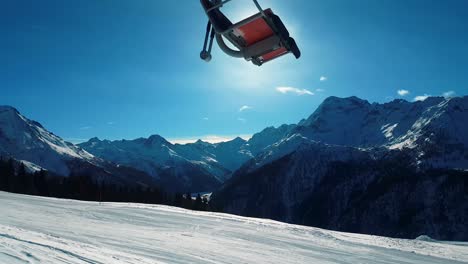 Valley-with-lake-surrounded-by-mountains-with-a-cable-way-seat-passing-in-front-of-the-sun-and-the-blue-sky