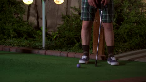 a close up of a purple mini golf ball getting hit with a club and the shot is horrible and the ball comes rolling back to the golfer