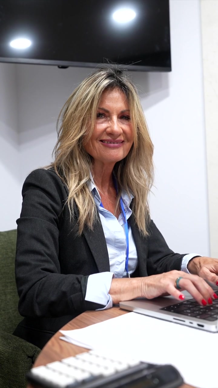 Donna d'affari matura sorridente lavora al laptop in ufficio.