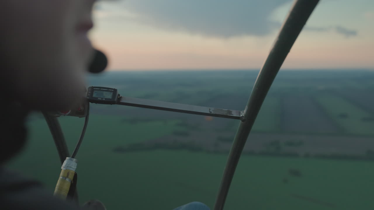 close up of pilot wearing headset and gloves gripping paraglider frame while scanning horizon sunset sky vivid green farmland below immersive flight control shot