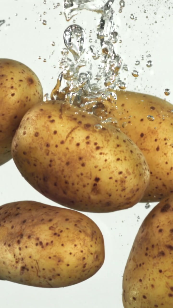 Patate fresche e crude che cadono in acqua limpida con bolle