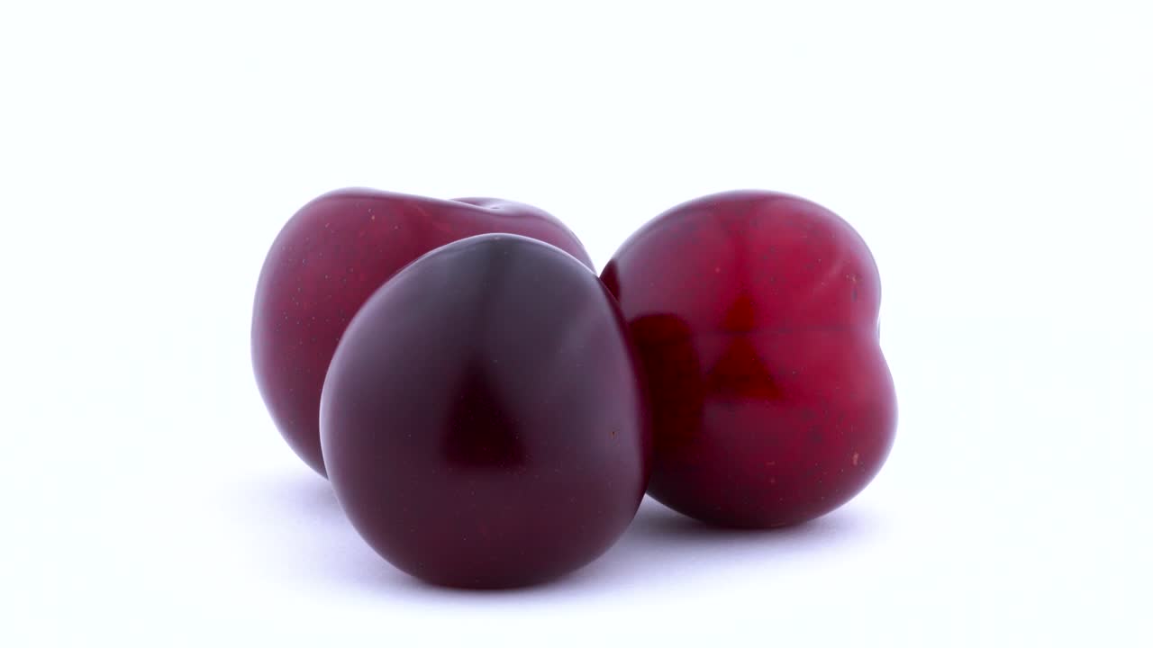 tres grandes ciruelas púrpura girando en el tocadiscos, aisladas en el fondo blanco, de cerca.