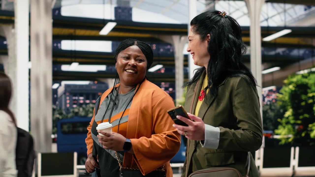 Friends walking through bus terminal with takeaway coffees and laughing