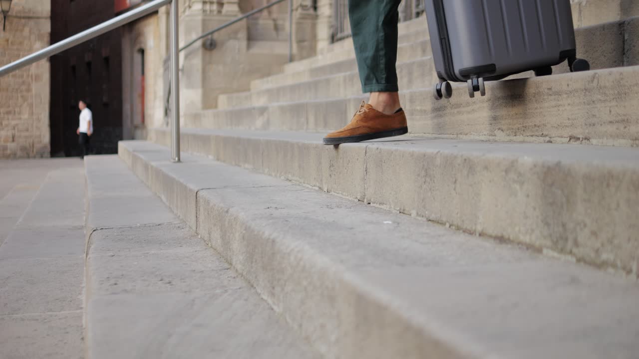 Person with suitcase walking up stone stairs in city