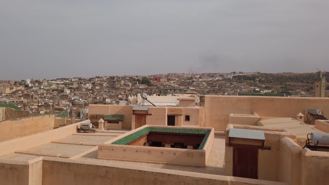 Veduta panoramica dal tetto sulla storica Medina di Fes, Marocco, con case tradizionali, tetti con tegole verdi e un minareto di moschea che si erge sopra il denso paesaggio urbano nordafricano.