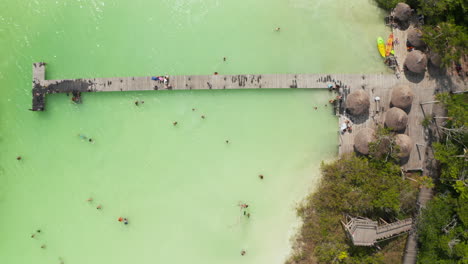 Aerial-birds-eye-overhead-top-down-zooming-view-of-wooden-pier-above-pastel-green-water.-People-enjoying-time-at-water-in-tropical-destination.-Kaan-Luum-lagoon,-Tulum,-Yucatan,-Mexico