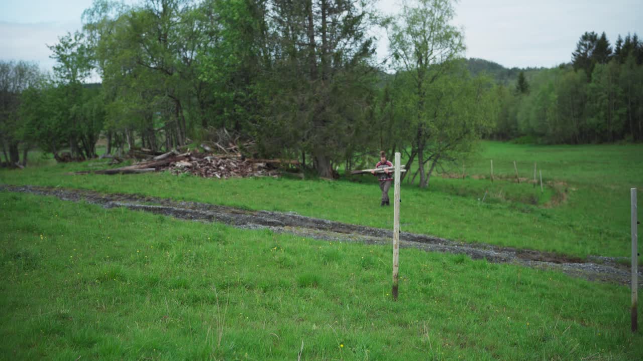 hombre llevando postes de valla en el campo.
