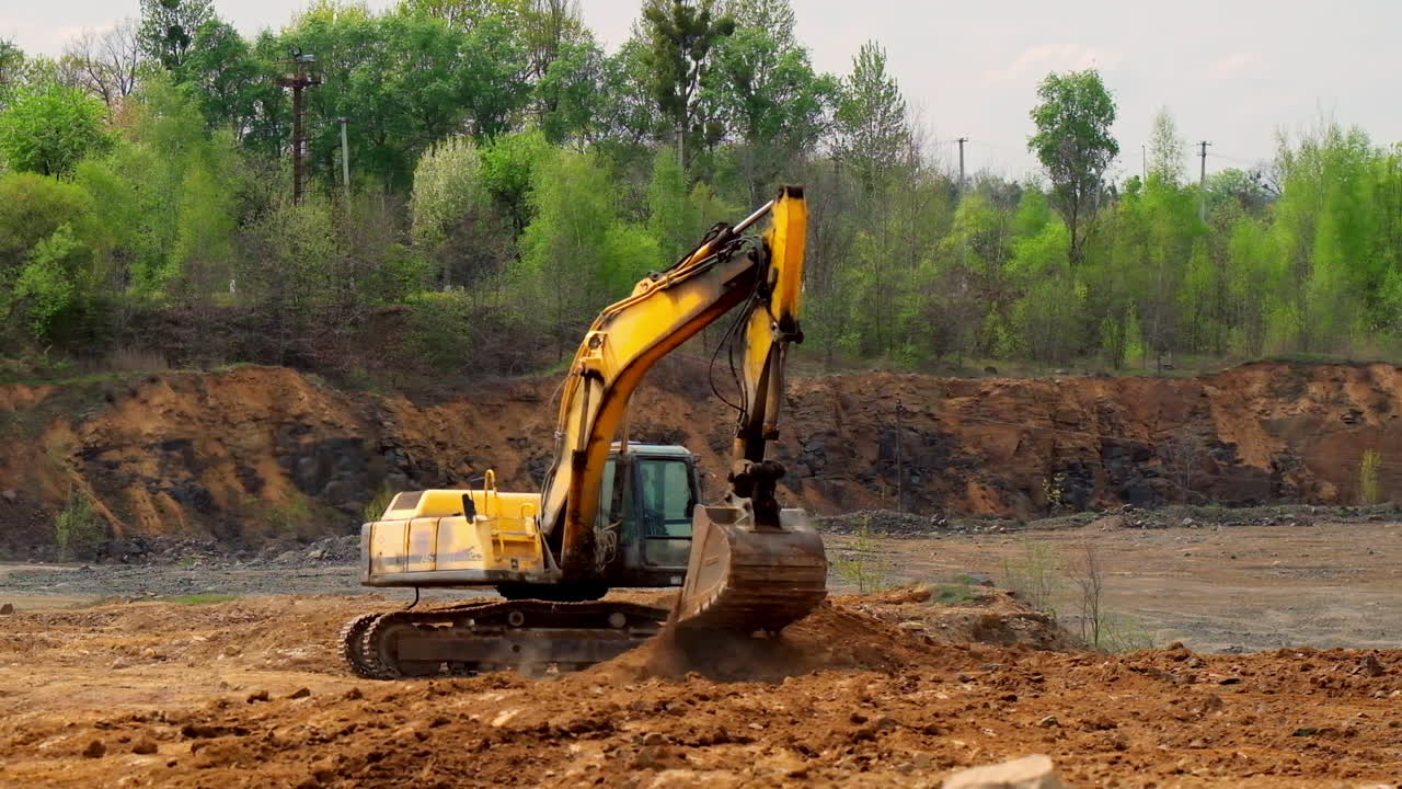 Earth moving equipment. Yellow excavator digging the ground. Excavator bucket scoops up the soil on nature background. Slow motion.