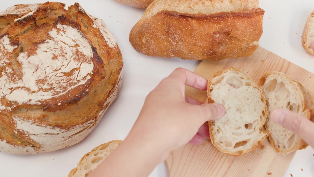Top-down view of hands organizing fresh crusty bread slices on a light wooden board.