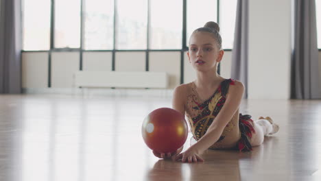 niña joven en leotardo practicando gimnasia rítmica con una pelota en un estudio 2