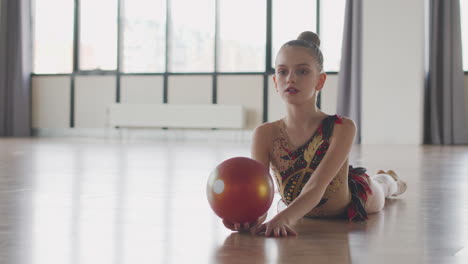 young girl in leotard practising rhythmic gymnastic with a ball in a studio 2