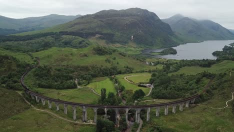 aerial: train approaches iconic curving glenfinnan viaduct, scotland