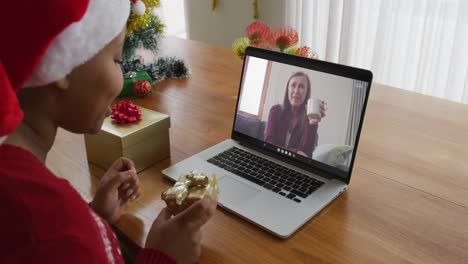 Mujer-Afroamericana-Con-Gorro-De-Papá-Noel-Usando-Una-Computadora-Portátil-Para-Una-Videollamada-Navideña,-Con-Un-Amigo-En-La-Pantalla