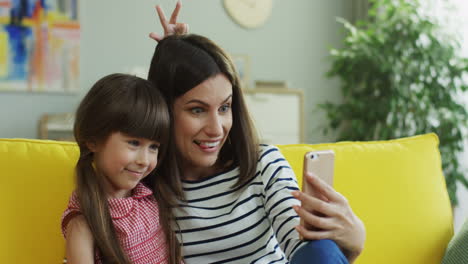 Nahaufnahme-Der-Lächelnden-Mutter-Und-Tochter,-Die-Ein-Lustiges-Selfie-Auf-Dem-Smartphone-Auf-Der-Gelben-Couch-Machen