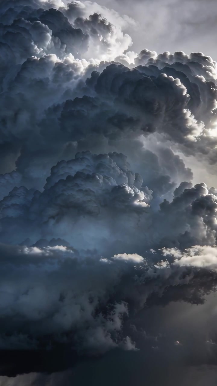 Video vertical: Nube cumulonimbus formándose y elevándose por convección en el cielo, con el sol retroiluminando sus cumbres.