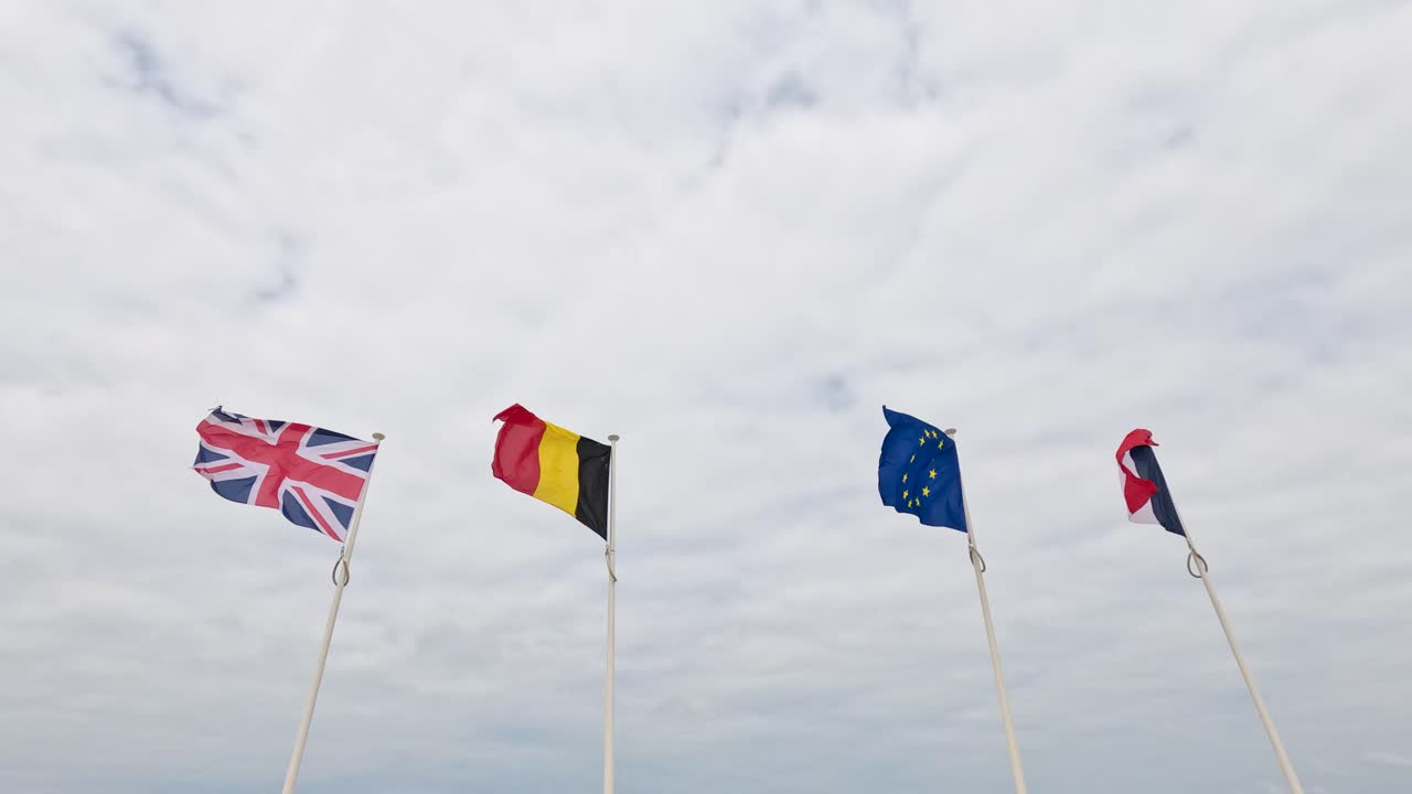 Four national flags wave in strong wind on a cloudy beach at Malo-les-Bains, France