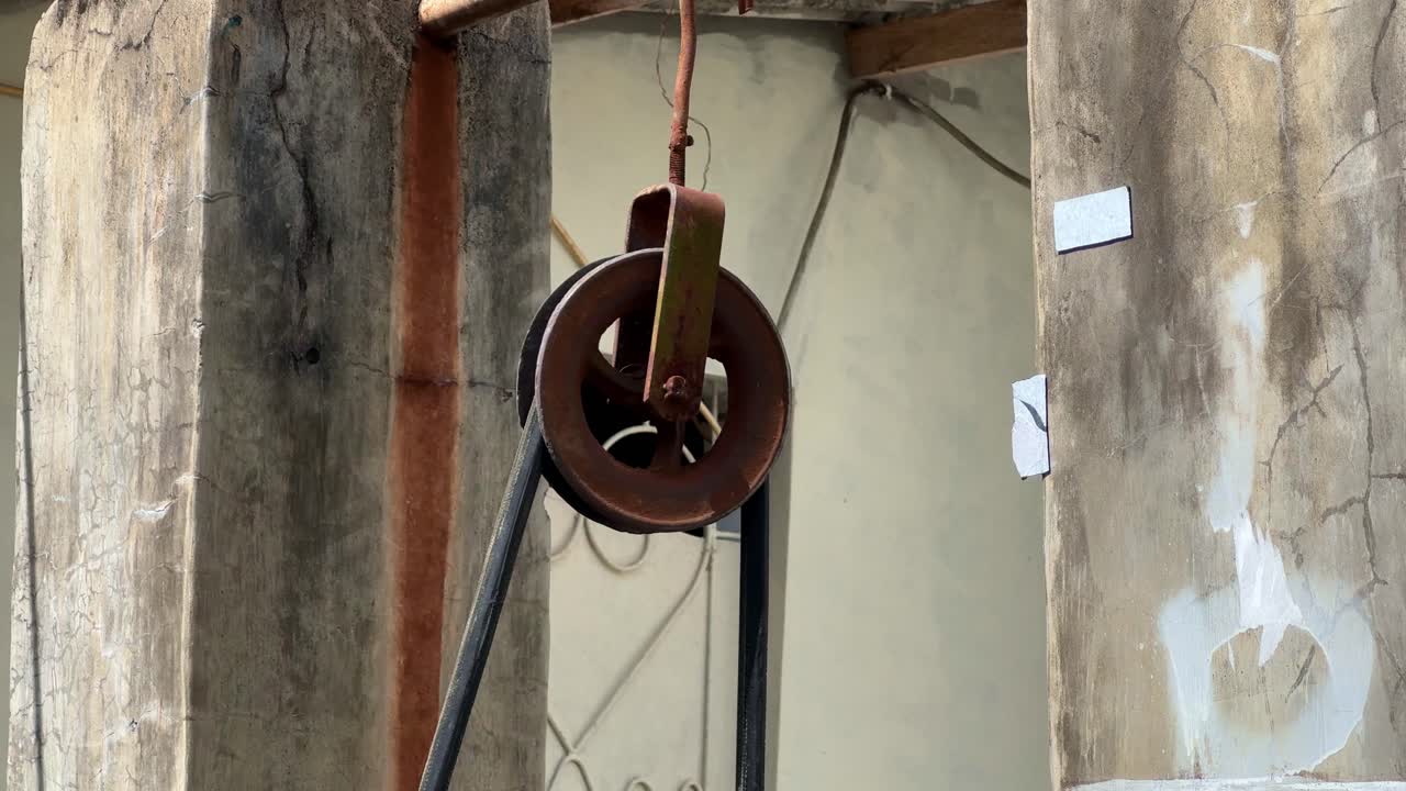 close-up shot of a manual crane pulley rotating as the belt is pulled, movement of the old, rusted wheel mechanism. Weathered metal parts, Manual Pulley for drawing water from the well