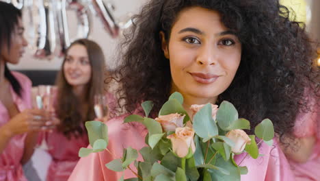 close up view of muslim woman holding bouquet and wearing pink silk nightdress smiling and looking at camera