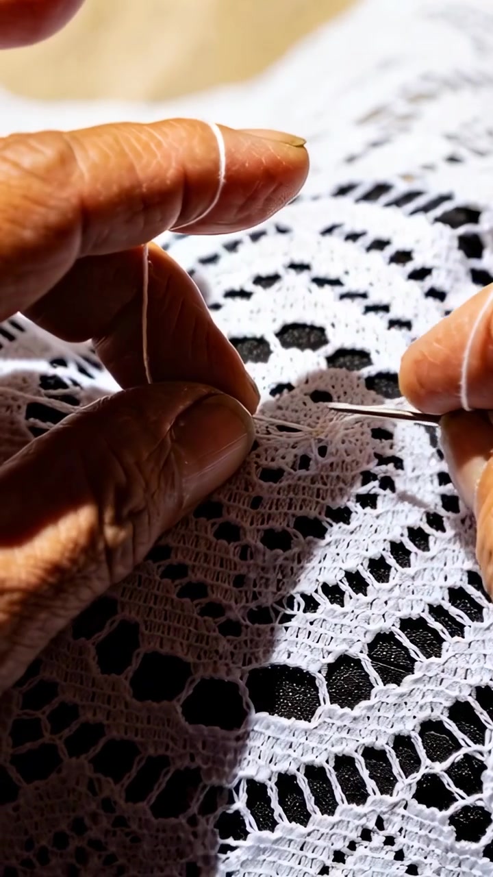 Vertical video: Inserting fine needle, hands repairing motif on doily at table with white thread