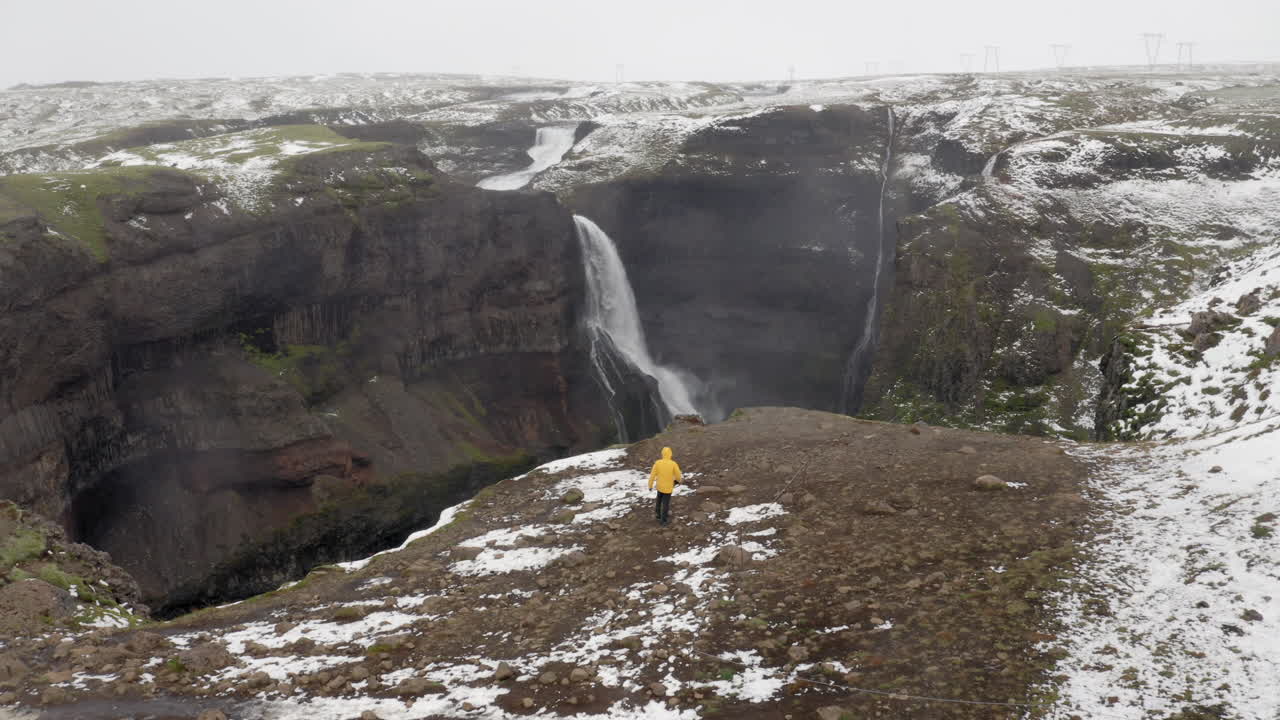 antena: un hombre caminando cerca del borde de un acantilado hacia la cascada granni en islandia