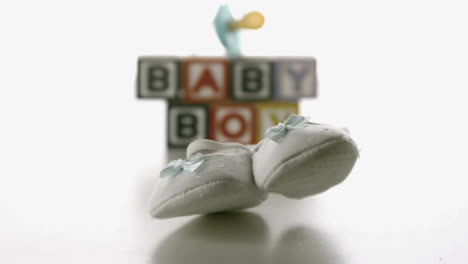 Baby-shoes-falling-in-front-of-blue-soother-and-baby-blocks