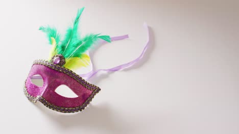 video of pink masquerade mask with green and yellow feathers on white background with copy space