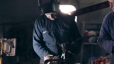 workers in protective workwear at mechanical hangar. workman in welding helmet joins two metal pieces together. dangerous work.